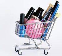 Miniature shopping cart filled with a variety of cosmetics on a white background.